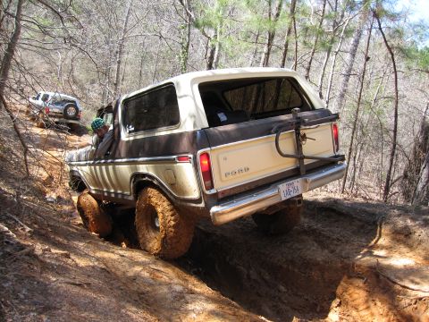 1993 Ford Bronco - Two SUVs navigate a challenging off-road trail with steep inclines and loose dirt.