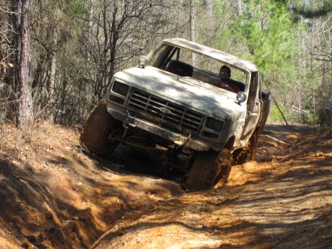 1993 Ford Bronco - A driver navigates a white Ford pickup truck through a challenging muddy off-road trail.
