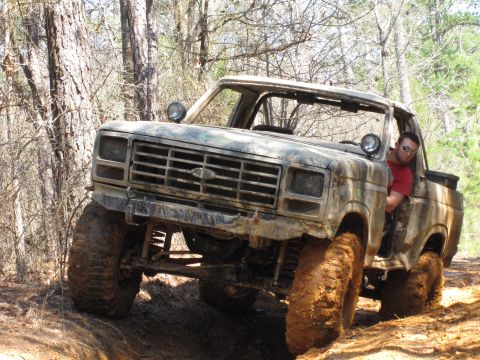 1993 Ford Bronco - A heavily modified 1980 Ford Bronco navigates a muddy trail in a wooded area.