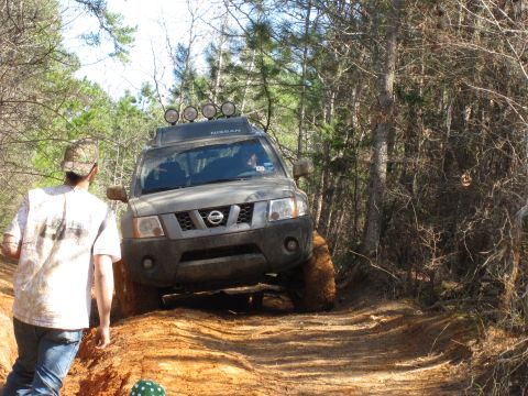 1993 Ford Bronco - A Nissan Xterra tackles an off-road trail, its tires covered in mud.