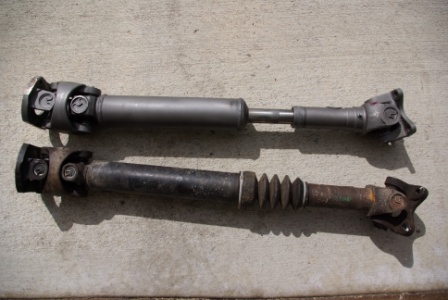 1995 Ford Bronco - Two driveshafts are laid out on a concrete surface, one showing signs of wear and rust.