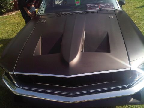 1986 Ford Bronco - A person is cleaning the hood of a car with a prominent hood scoop and chrome accents.