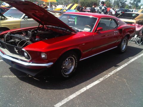 1986 Ford Bronco - A red 1969 Ford Mustang is displayed with its hood up at a car show.