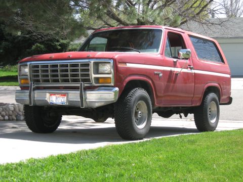 1981 Ford Bronco - Driver-side 3/4 front view of a red full-size two-door Ford Bronco with removable hardtop parked on a suburban driveway, its single-stage p…