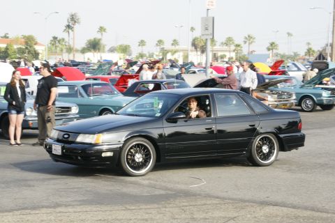 1992 Ford Taurus - A black 1992 Ford Taurus is parked at a car show with other vehicles in the background.