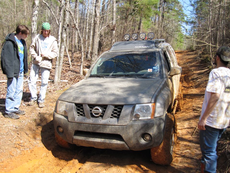 Nissan Xterra stuck in mud on a wooded trail with three people nearby