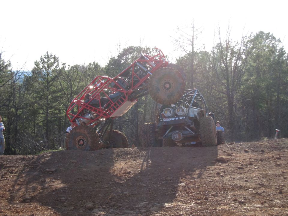 Red buggy on its side, gray buggy behind it, both on muddy terrain with trees in background