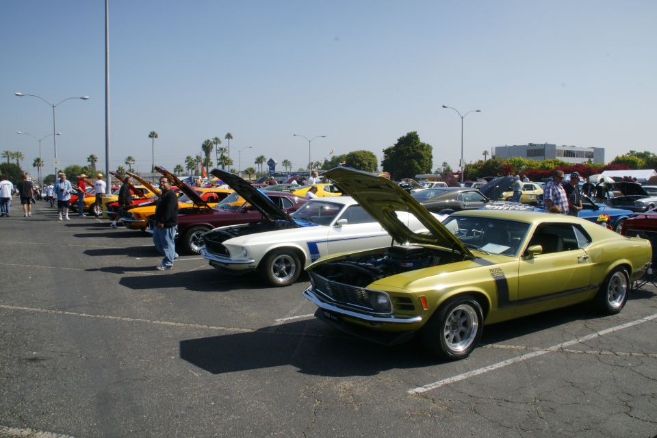 Yellow 1970 muscle car with hood open, parked in a lot with other classic cars