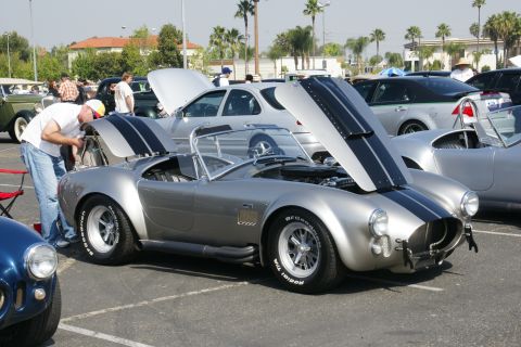 1992 Ford Taurus - A man inspects the engine of a silver Shelby Cobra at a car show, with another Cobra visible.