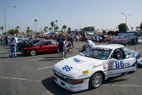 1992 Ford Taurus - A white race car with racing decals and the number 86 is parked in a lot with other vehicles and spectators.