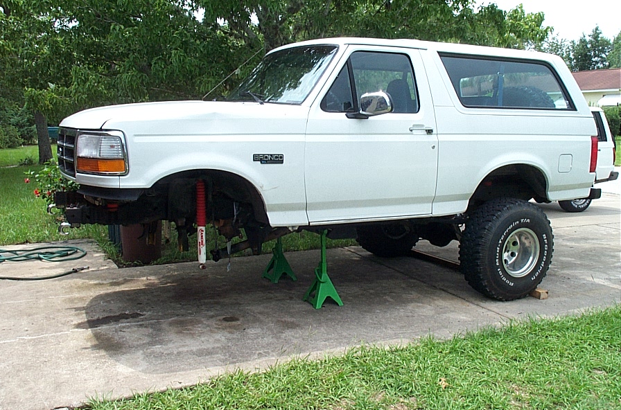 White Ford Bronco on jack stands with front wheel removed in a backyard driveway