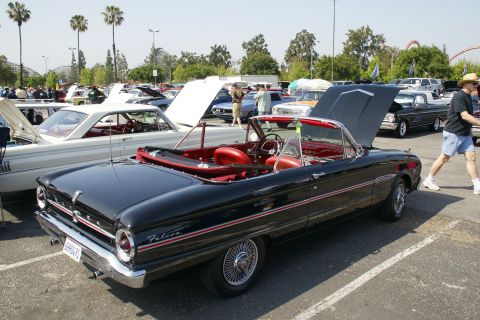 1992 Ford Taurus - A classic black convertible with a red interior is displayed at a car show, with other vehicles and palm trees in the background.