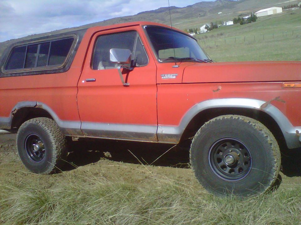 Red 1978 Ford Bronco parked on dirt with grass and hills in background