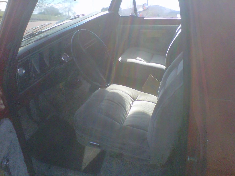 Interior view of a vehicle, showing the dashboard, steering wheel, and front seats. The seats have a plaid pattern