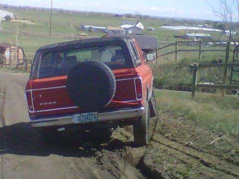 1978 Ford Bronco - 1978 Ford Bronco navigating a muddy off-road trail with a rural landscape in the background.