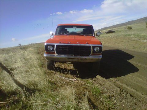 1978 Ford Bronco - Front view of an orange truck parked on a dirt road with another vehicle visible in the distance.