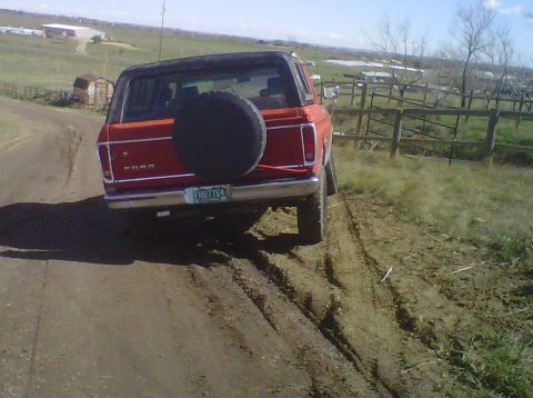1978 Ford Bronco - This red Ford Bronco is shown from the rear, driving on a dirt road with a spare tire mounted on the tailgate.