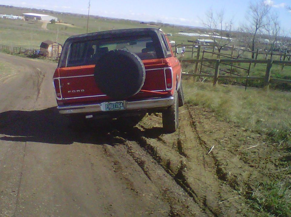 Red 1978 Ford Bronco on a dirt road, spare tire on back