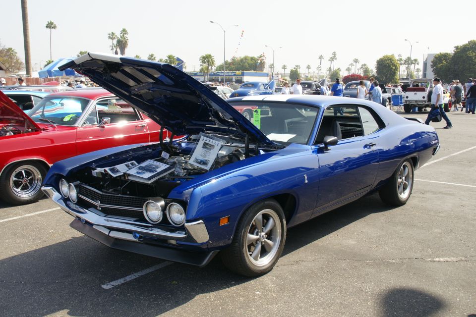 Blue 1970 Ford Torino GT with hood open, parked next to a red car at a car show