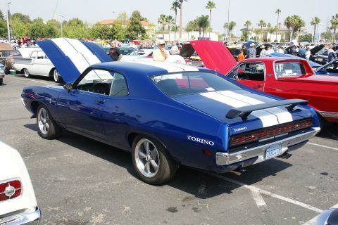 1992 Ford Taurus - Blue Ford Torino coupe with white racing stripes and a rear spoiler is parked at an outdoor car show.