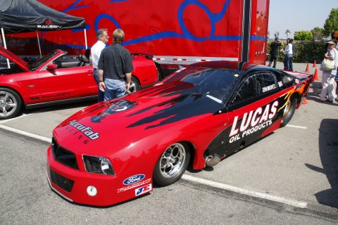 1992 Ford Taurus - Drag racing car with sponsor decals parked at an event with other vehicles and a trailer.