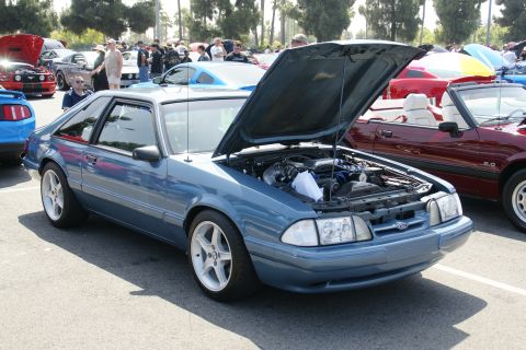 1992 Ford Taurus - A blue coupe with its hood open, parked at an outdoor car show.