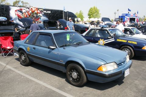 1992 Ford Taurus - This blue police car, possibly a 1992 Ford Mustang, is displayed at a car show. Another police car is visible behind it.