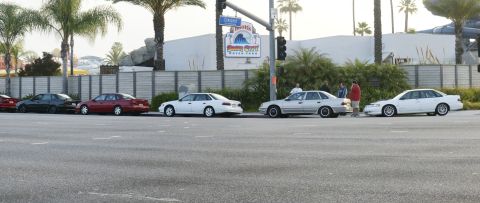 1992 Ford Taurus - Several sedans are parked along a street in front of a building with palm trees.