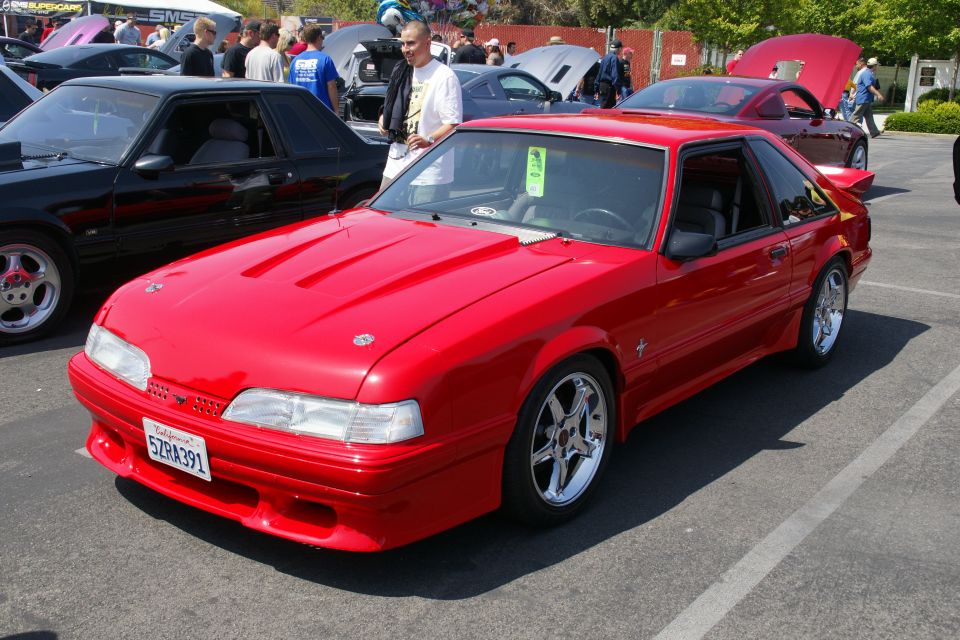 Red coupe with a hood scoop and chrome wheels parked on asphalt