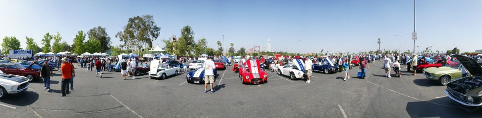 Car show scene with many classic cars and attendees under a clear blue sky