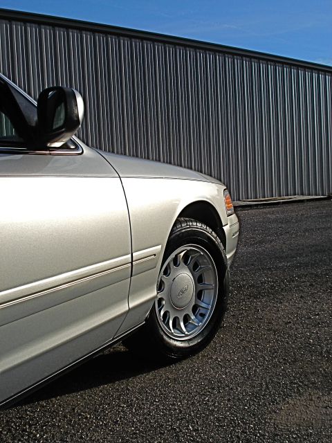 2000 Ford Crown Victoria - A silver 2000 Ford Crown Victoria is shown from the front three-quarter angle, highlighting its wheel and side bodywork.