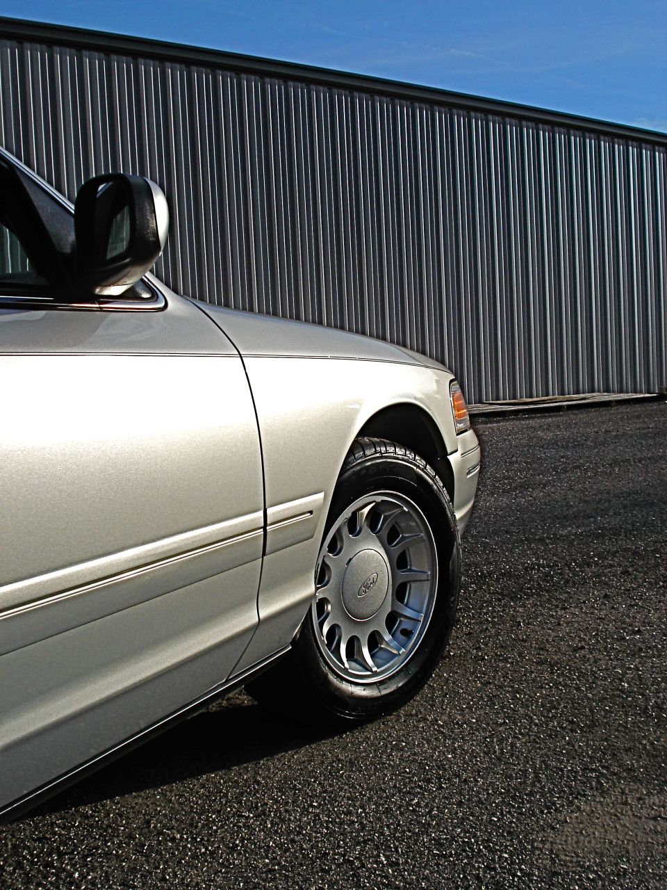 Silver 2000 Ford Crown Victoria 3/4 front view showing wheel and side panel