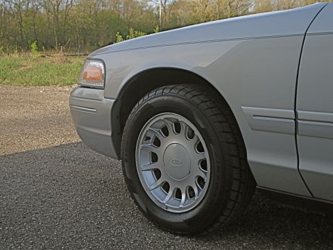 2000 Ford Crown Victoria - Front fender and wheel of a silver 2000 Ford Crown Victoria, parked on a gravel road with trees in the background.