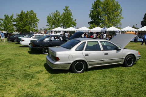 1992 Ford Taurus - A silver 1992 Ford Taurus sedan is displayed with its hood open at an outdoor car show, with other vehicles lined up behind it.