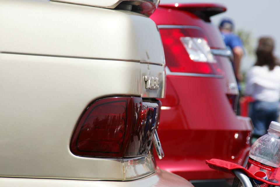 Close up of the rear of a tan car next to a red car. The tan car has a spoiler and a chrome trim piece above the taillight
