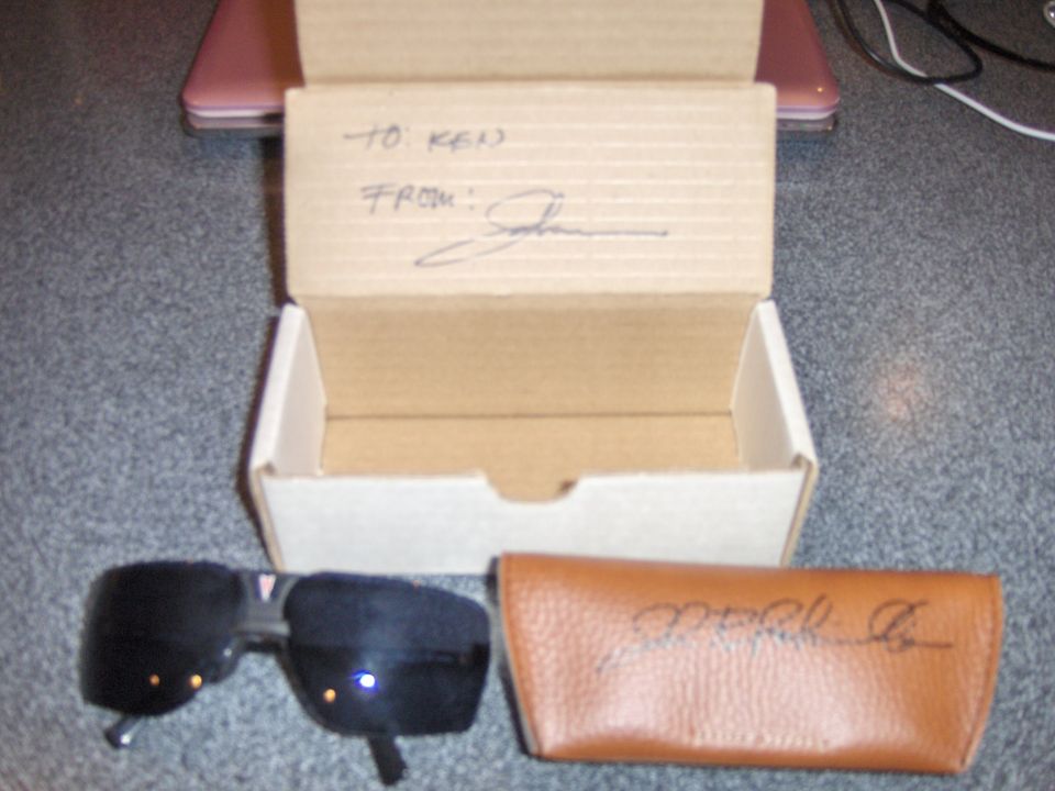 Black sunglasses next to a brown leather case and an open cardboard box with writing