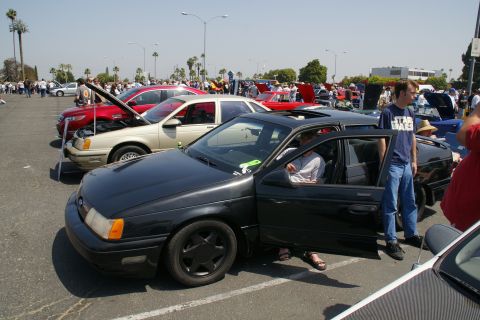 1992 Ford Taurus - A black sedan is parked with its door open at an outdoor car show.