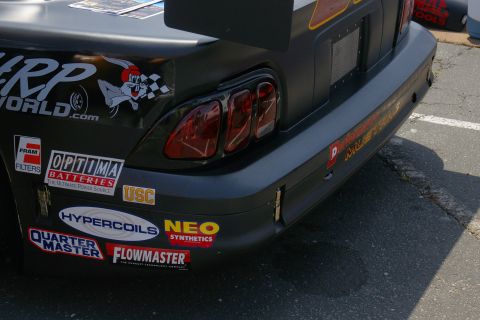 1992 Ford Taurus - The rear of a black race car is shown, covered in sponsor decals, with a checkered flag and cartoon rabbit sticker on the left side.