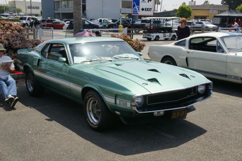 1992 Ford Taurus - A green 1969 Ford Mustang Shelby GT500 is parked next to a white Ford Mustang GT at an outdoor car show.