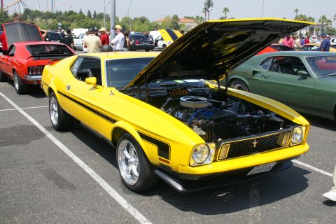 1992 Ford Taurus - A yellow 1973 Ford Mustang Mach 1 is displayed with its hood open, revealing the engine, at a car show.