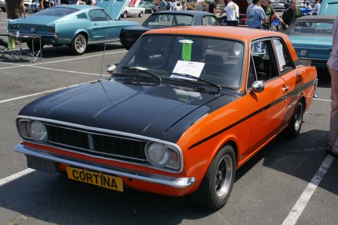 1992 Ford Taurus - This two-door coupe features a striking orange and black paint scheme, with a prominent yellow license plate reading 'Cortina'.