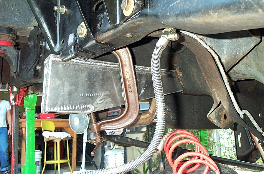 Welded steel crossmember bracket bolted to a frame rail with a copper line and braided hose nearby