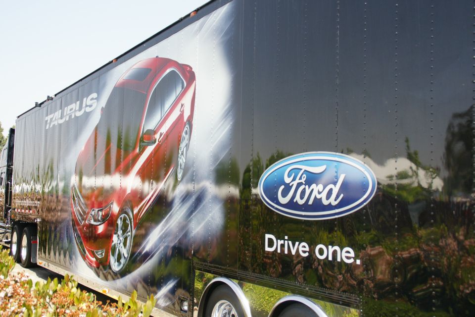 Trailer with a graphic of a red Ford Taurus and Ford logo. Text says 'Taurus' and 'Drive one.'