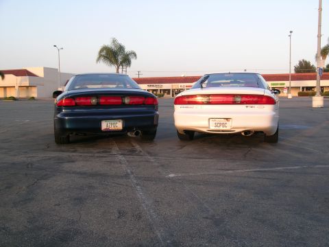 1993 Ford Probe - Two Ford Probe cars, a blue one and a white one, are parked in a lot, viewed from the rear.