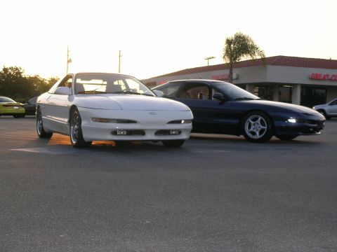 1993 Ford Probe - Two Ford Probes are parked in a lot during sunset, with a building and palm tree visible behind them.