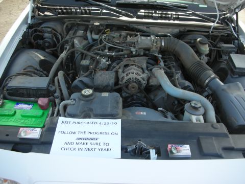 2004 Ford Crown Victoria - Engine bay of a white car with a handwritten sign reading 'JUST PURCHASED 4/23/10 FOLLOW THE PROGRESS ON SUPERMOTORS'.