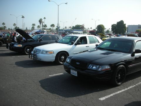 2004 Ford Crown Victoria - Three Ford Crown Victoria police cars are parked in a lot, with one black car's hood open.