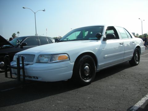 2004 Ford Crown Victoria - A white police car is parked on asphalt under a bright sky.