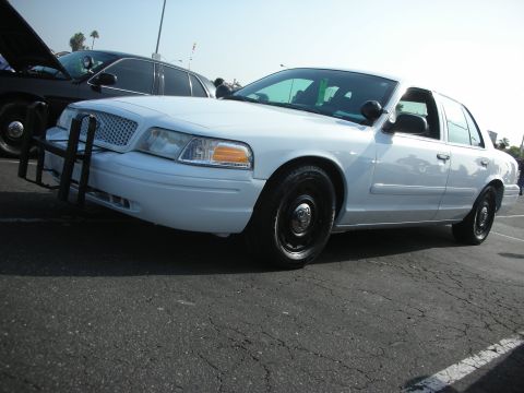 2004 Ford Crown Victoria - A white Ford Crown Victoria with a push bar is parked on asphalt, with another car visible behind it.