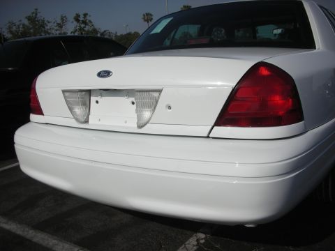 2004 Ford Crown Victoria - The rear of a white 2004 Ford Crown Victoria is shown, with a black vehicle partially visible to the left.